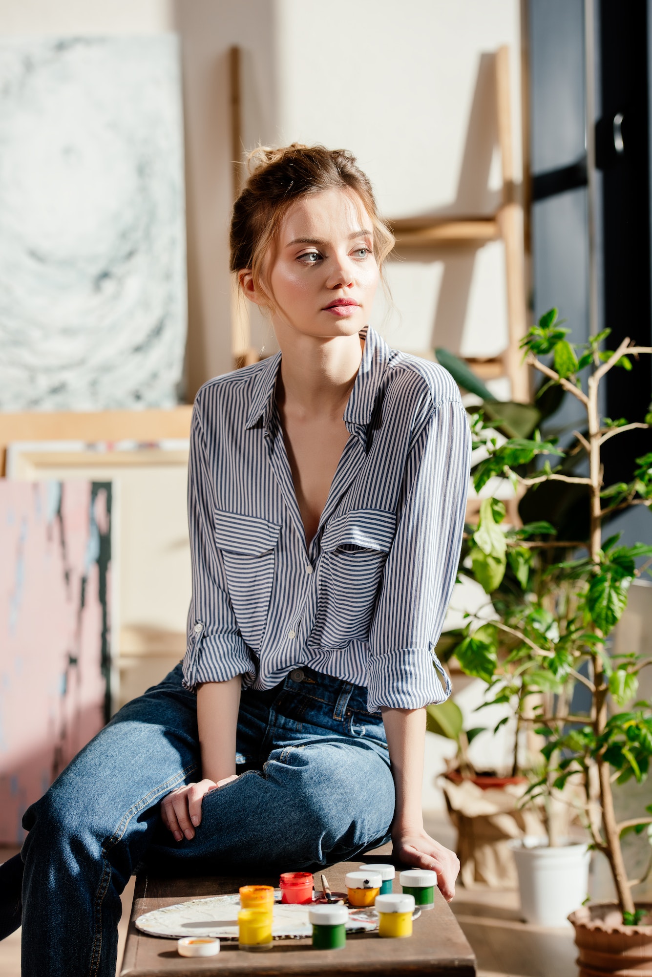 young female artist sitting on bench with paints and looking away